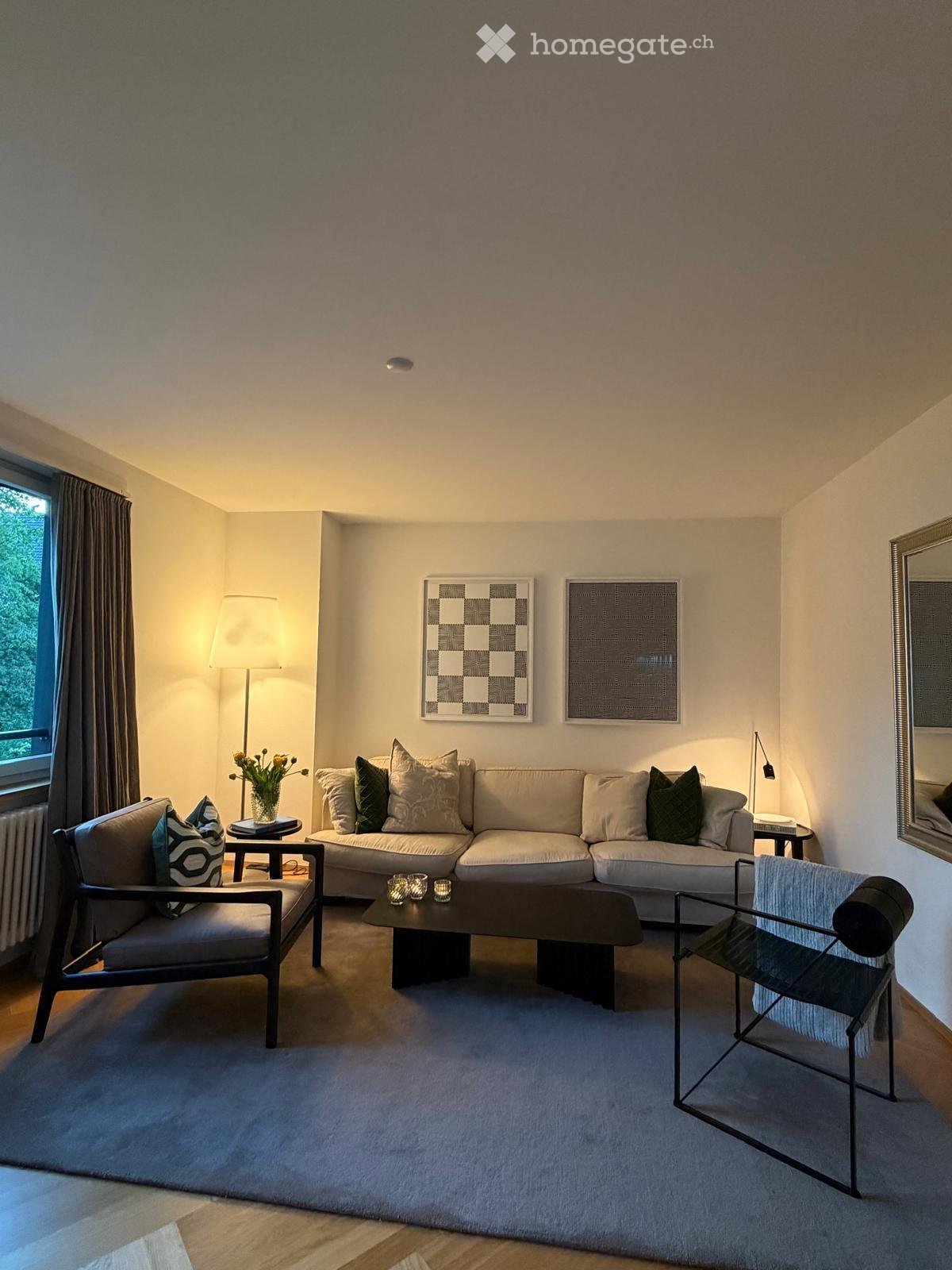 Modern living room with a large sectional sofa, coffee table, two armchairs, a floor lamp, and decorative artwork on the walls.