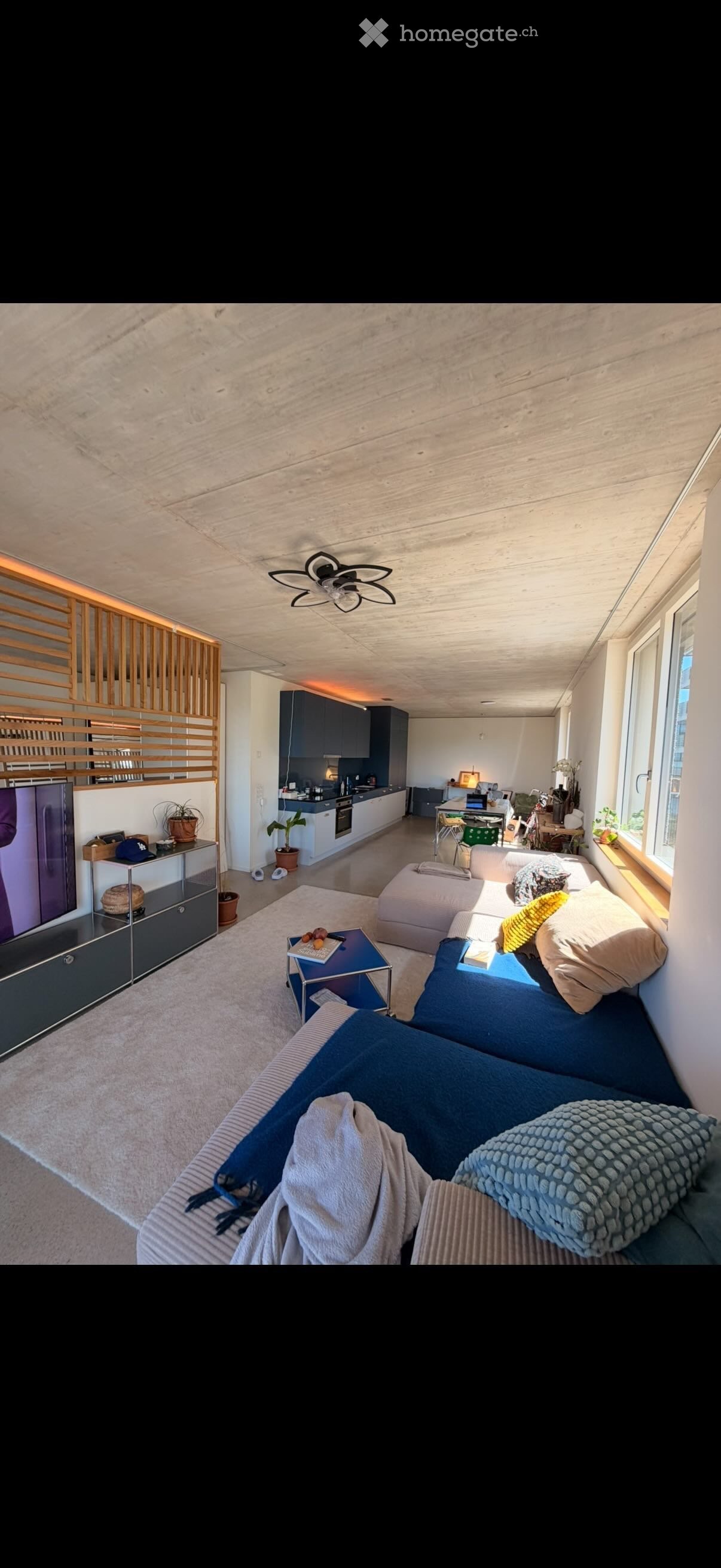 Modern open-plan living and dining area with a sectional sofa, coffee table, TV, and a small kitchen area with cabinets and appliances.