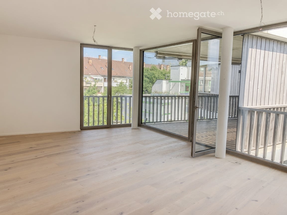 Empty room with wooden flooring, large glass doors leading to a balcony, and a view of the surrounding area.