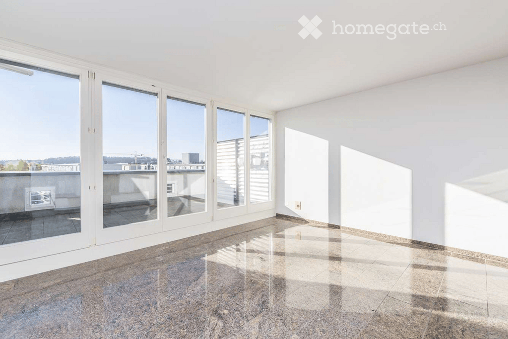 Empty room with large windows and a view of a balcony area. The floor is tiled, and the walls are white.