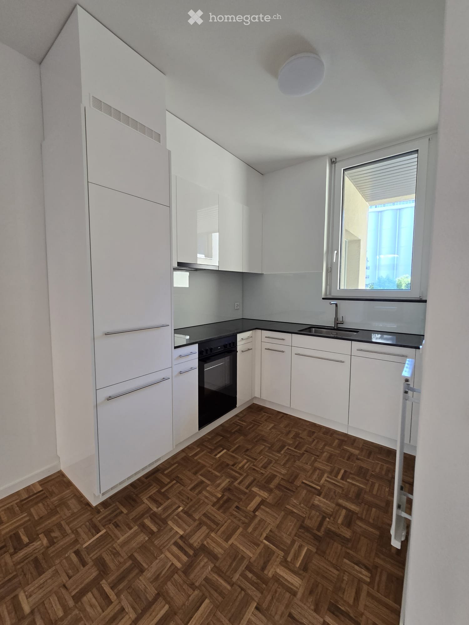 Modern kitchen with white cabinets, black countertops, and a wooden herringbone floor. Features an oven and a sink.
