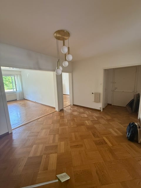 Empty room with wooden flooring, white walls, and a modern chandelier. No furniture or equipment present.
