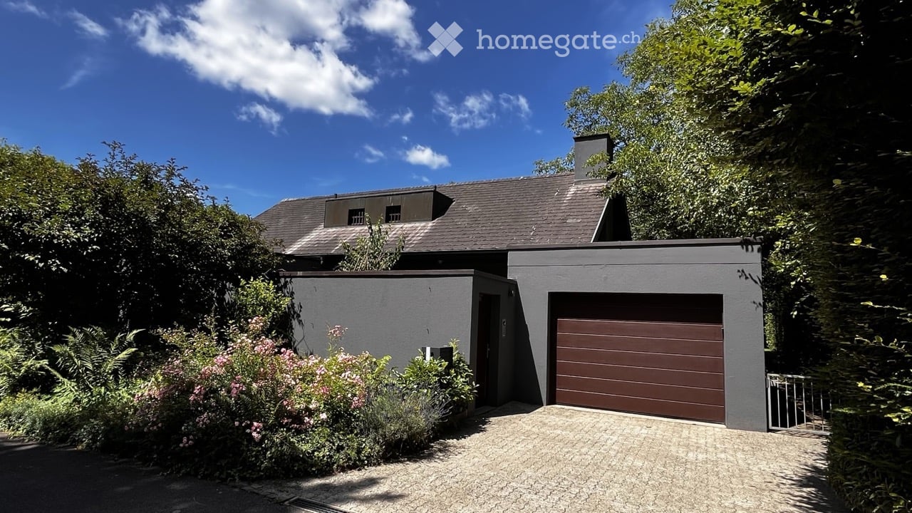 Modern two-story house with grey exterior, dark brown garage door, and surrounding greenery.