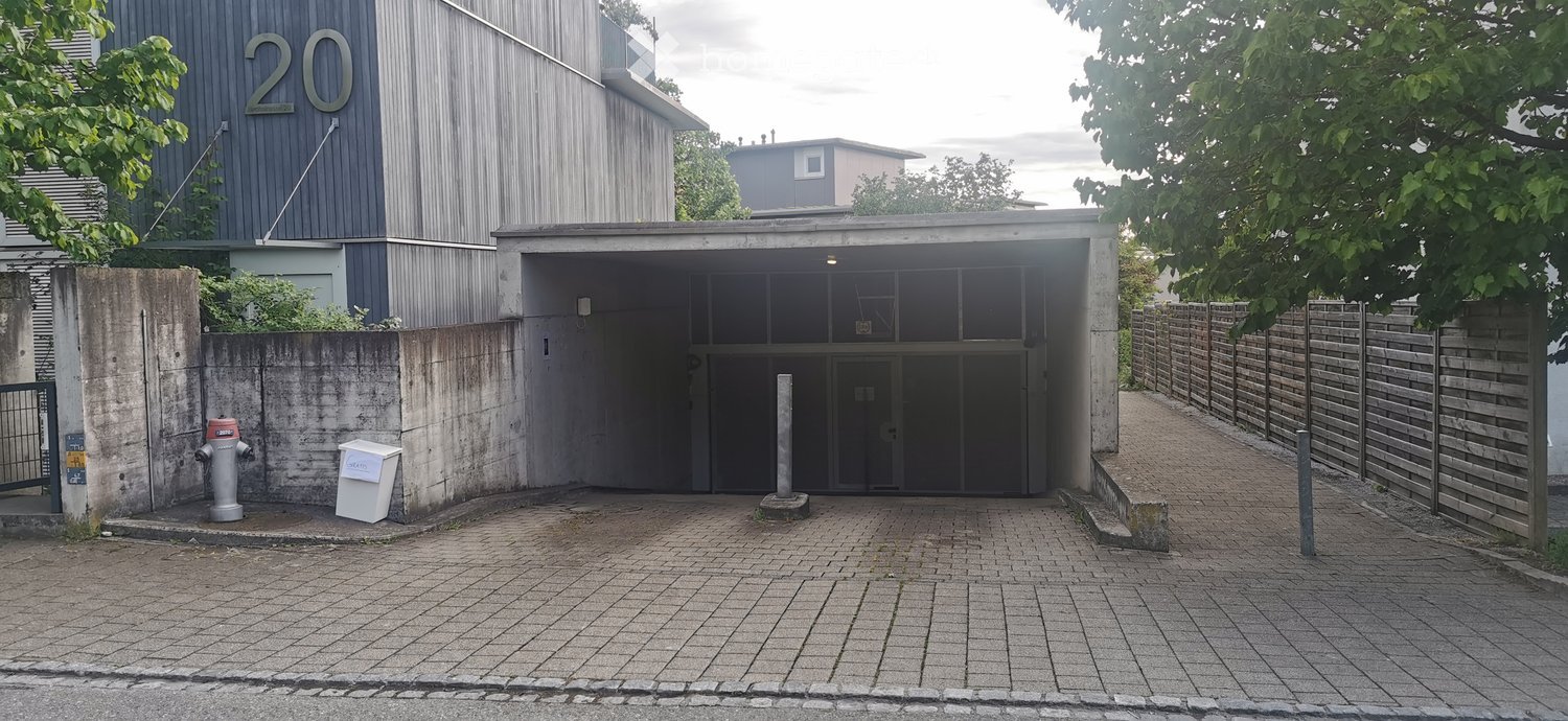 Building. Modern building entrance with a covered garage area, brick pavement, and a concrete wall on one side.
