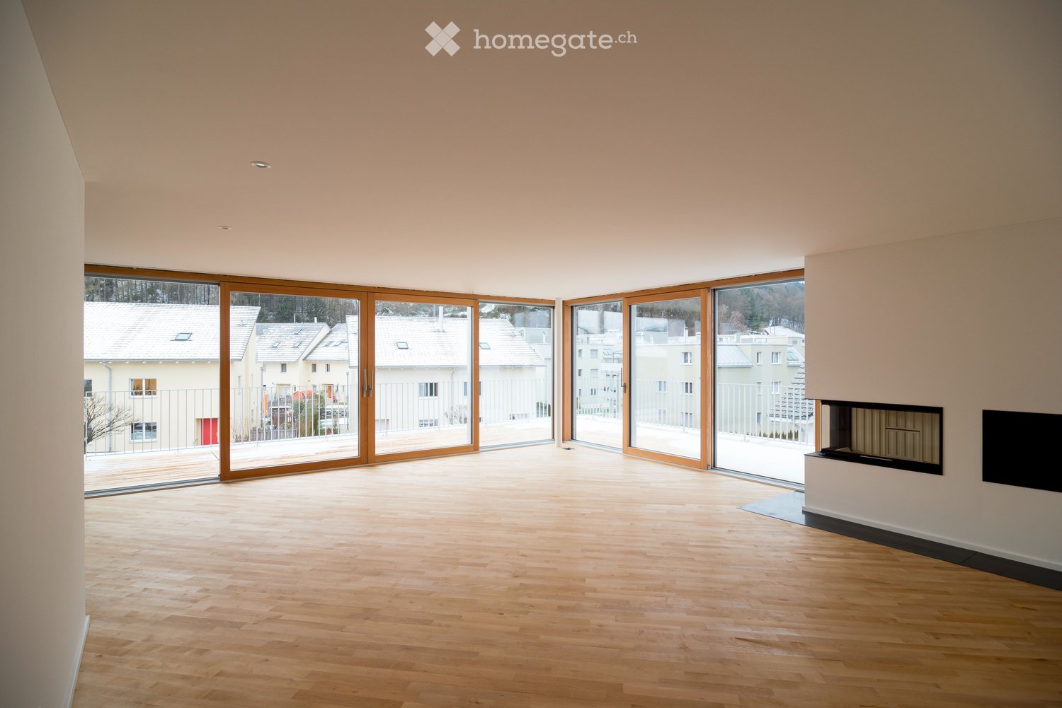 Bright, empty room with wooden flooring, large sliding glass doors leading to a balcony, and a fireplace on one wall.