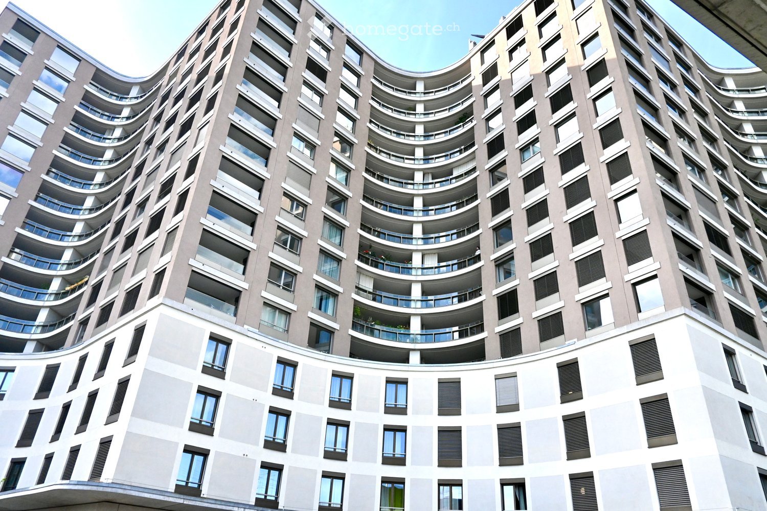 Modern high-rise building with curved balconies and large windows, featuring a mix of grey and white exterior walls and black shutters.