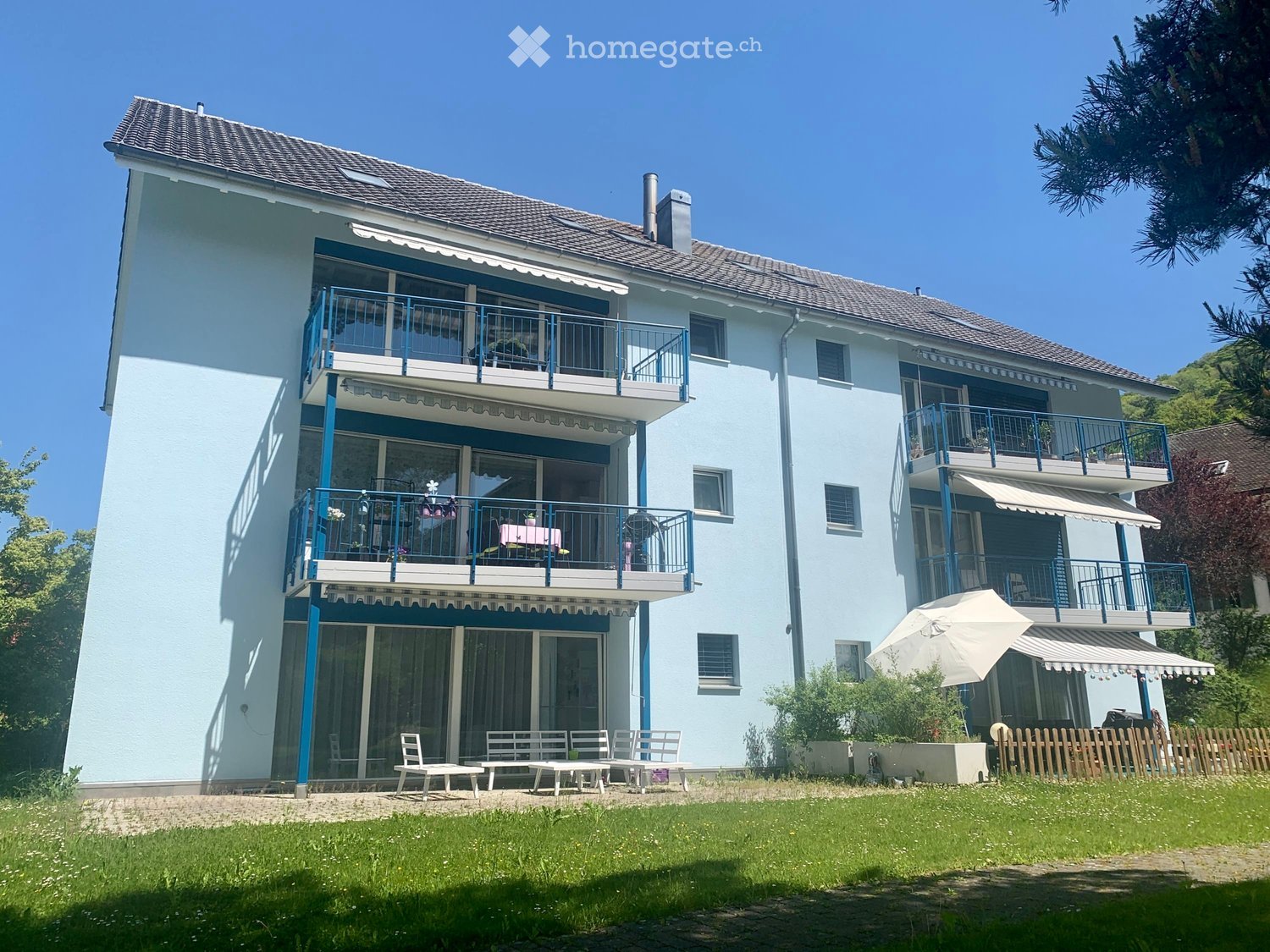 3 story house, light blue color, many balconies, white doors, white chairs