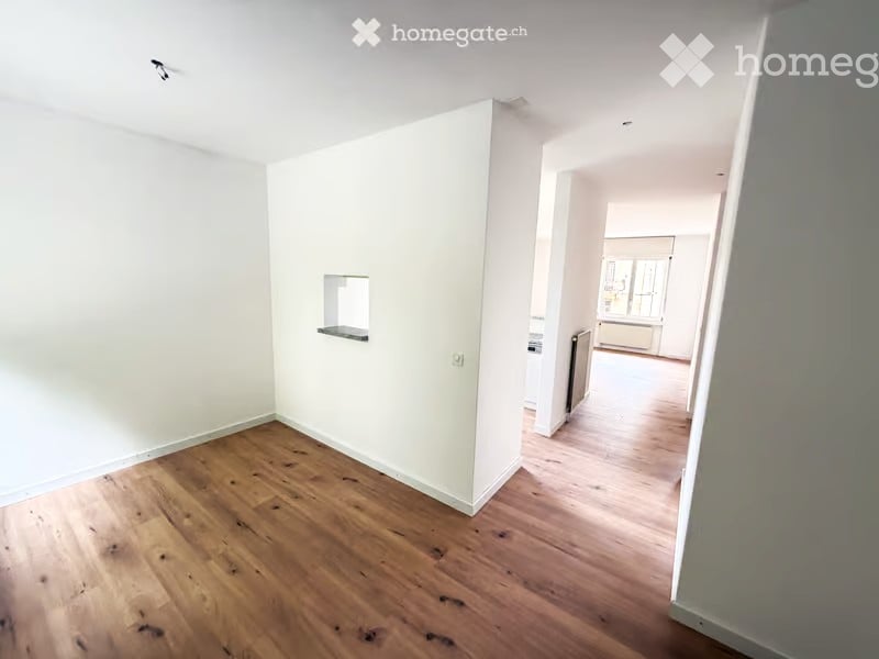 Empty room with wooden flooring and white walls, featuring a small built-in shelf and a visible doorway leading to another room.