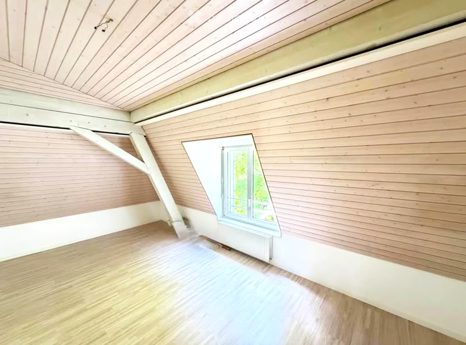 Empty room with wooden walls, ceiling, and floor, featuring a single window with a view of greenery outside.