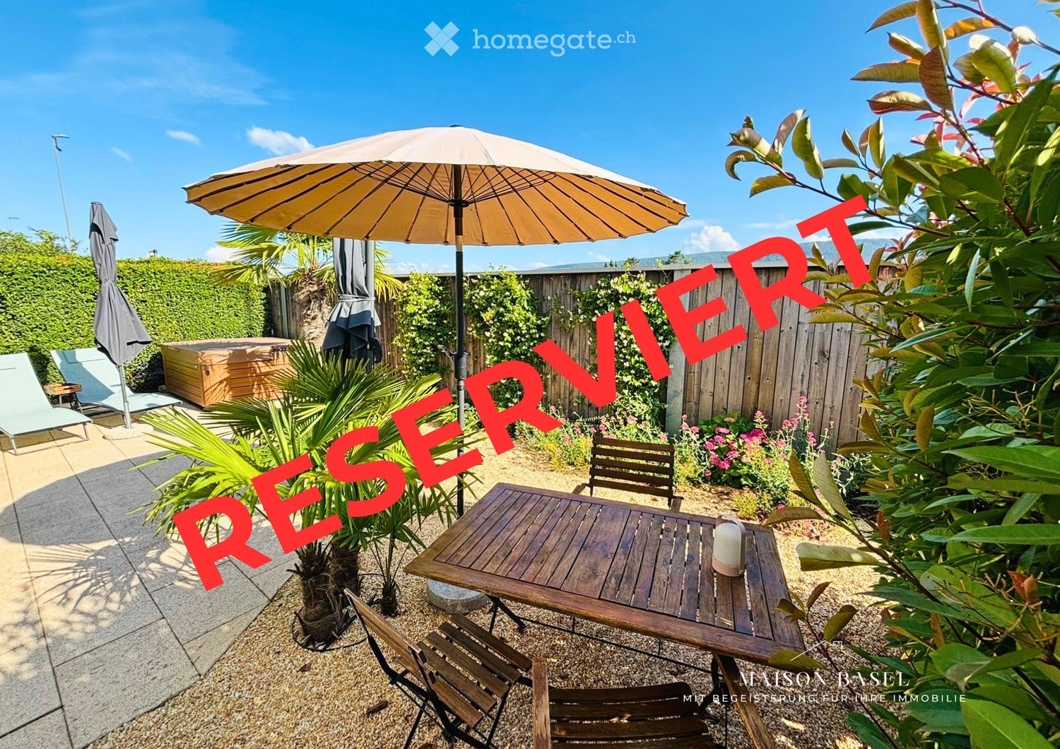 A well-maintained garden area with a wooden table, chairs, lounge chairs, a large umbrella, a wooden hot tub, and lush greenery.