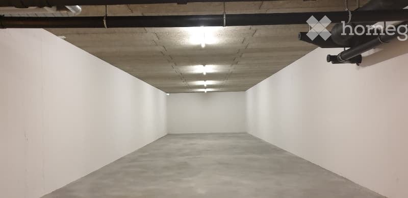 Empty basement garage with white walls and gray floor, exposed ceiling beams, and hanging pipes.