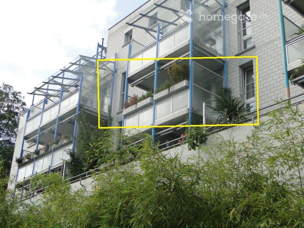 Modern multi-story building with balconies and greenery, featuring glass railings and potted plants.