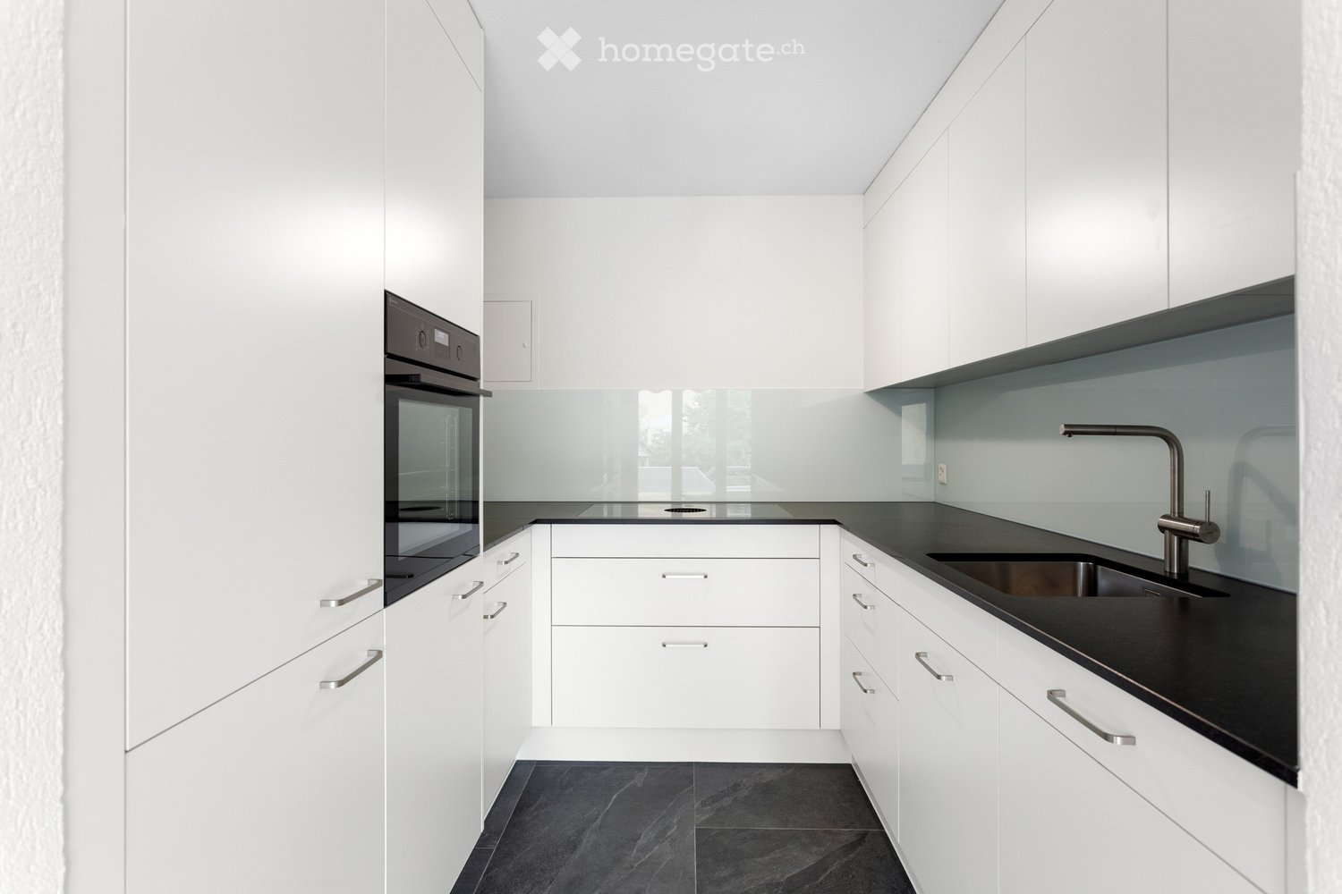 Modern kitchen with white cabinets, black countertops, stainless steel sink and faucet, and built-in oven.
