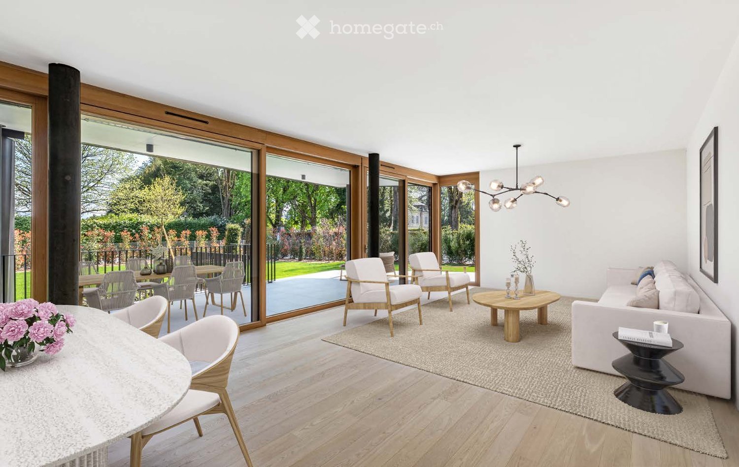 Modern living room with white walls, wooden floors, large glass doors opening to a garden, a white sofa, coffee table, chairs, and a chandelier.