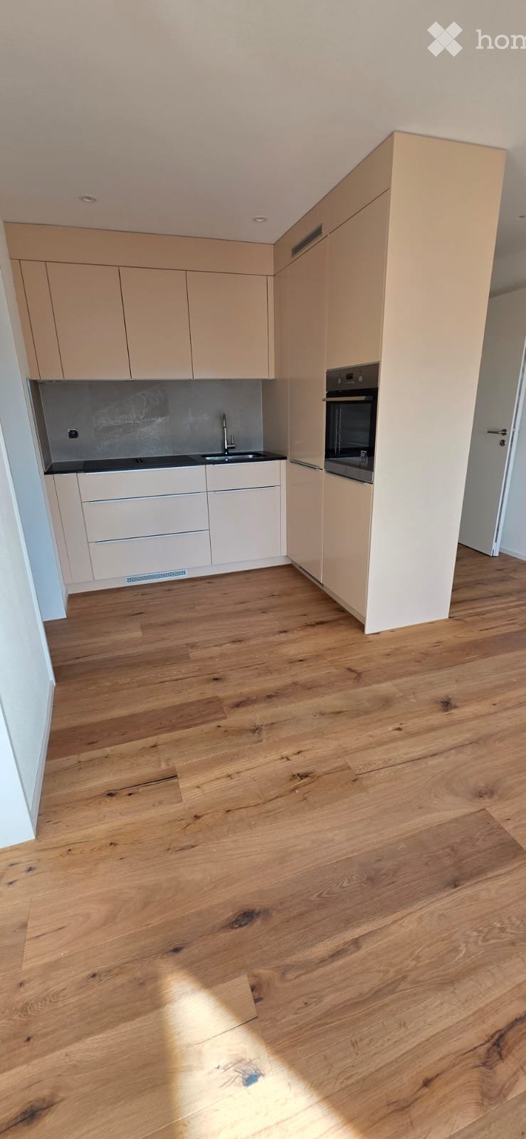 Modern kitchen with wooden floors, white cabinets, black countertops, and a built-in oven.