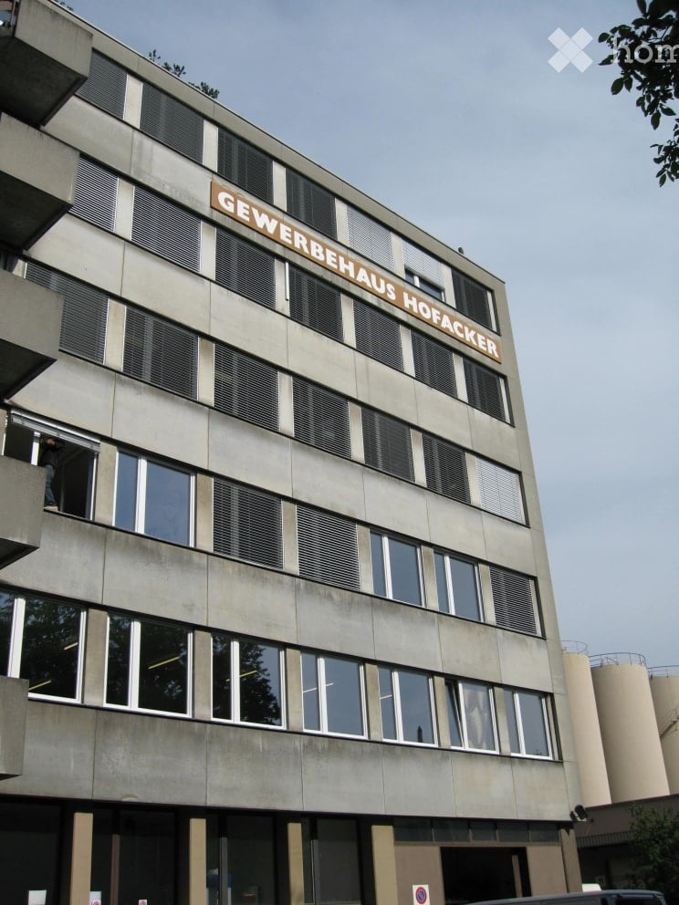 Multi-story commercial building with large windows and a sign reading "GEWERBEHAUS HOFACKER" on the facade.