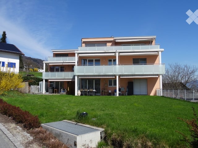 Two-story house with balconies, light pink facade, and a well-maintained green lawn in front.