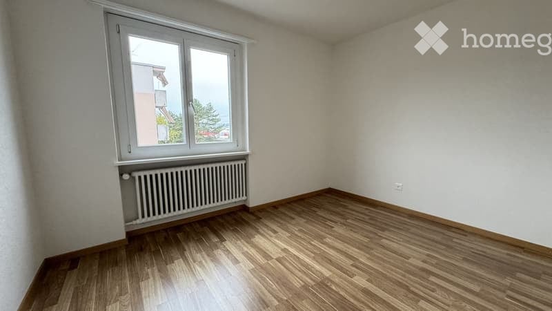 Empty room with wooden flooring, white walls, and a single window with a radiator below it.