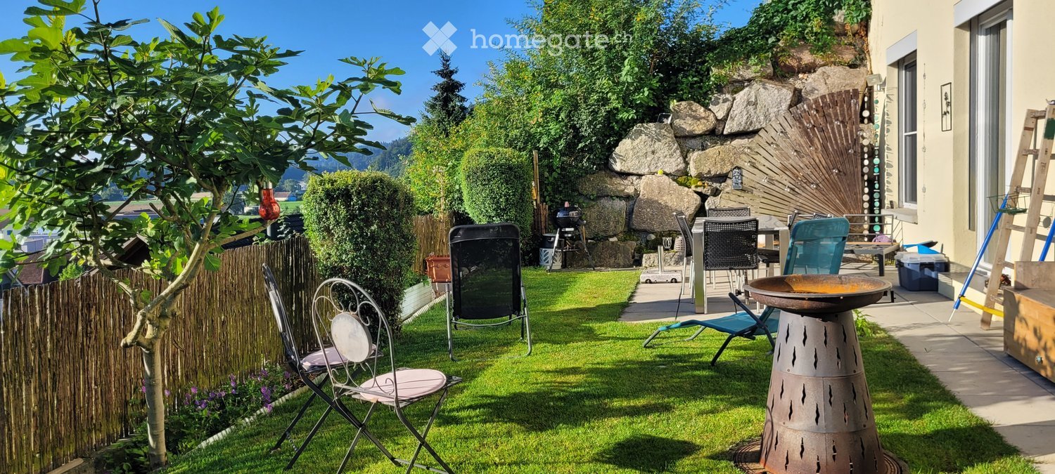Well-maintained garden with a stone wall, barbecue, outdoor seating area, and decorative elements.