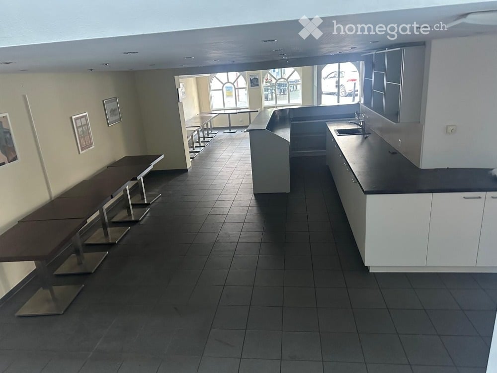 Empty room with tiled floor, white cabinets, black countertop, and several tables and chairs arranged in rows.