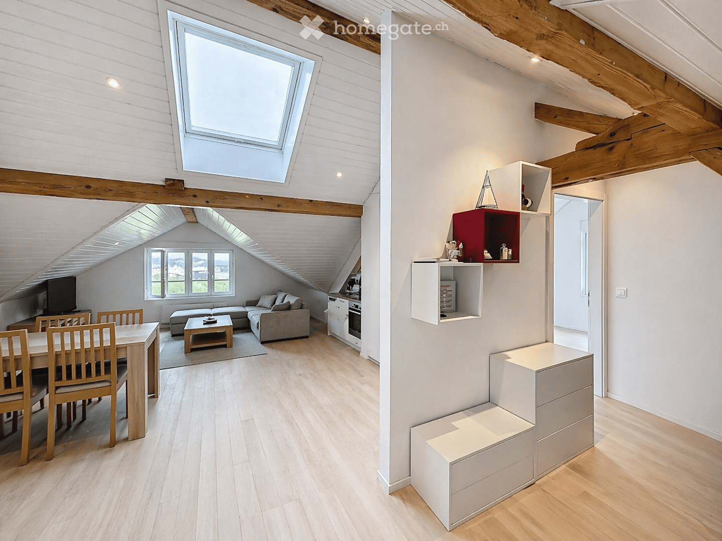 open-plan living room and dining area, wooden floor, white walls, skylight, dining table, chairs, couch, coffee table, TV, kitchen, shelves, storage drawers