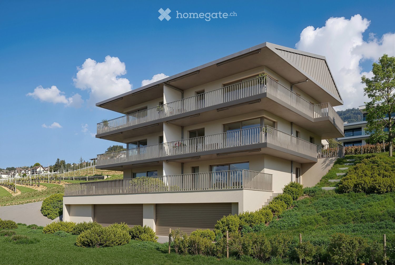 Modern two-story house with multiple balconies, situated on a hillside with well-maintained landscaping and a clear blue sky in the background.