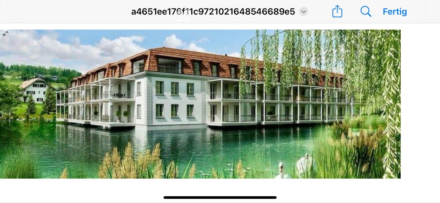 A large, modern building with a red-tiled roof and multiple balconies, situated on a waterfront with a calm lake and surrounding greenery.