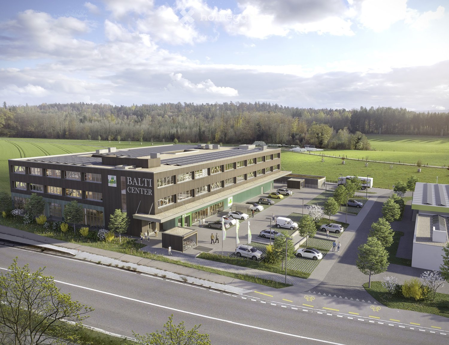 A modern multi-story building labeled "BALTI CENTER" with large windows, solar panels on the roof, and a parking lot with several cars. The surrounding area includes green fields, trees, and a paved road.