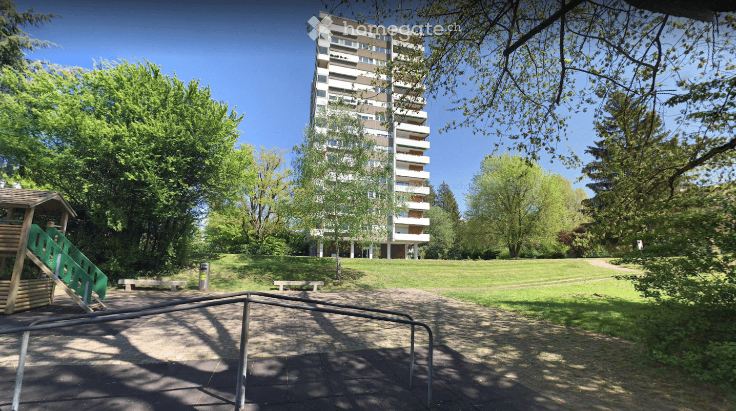 A park area with a playground, benches, and a multi-story residential building in the background.