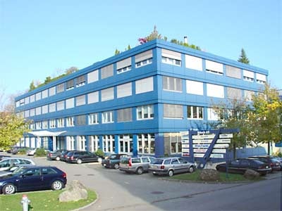 A multi-story blue building with white-framed windows, surrounded by a parking lot with several cars.