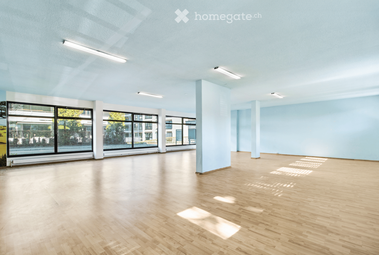large room, wooden floors, white walls, fluorescent lights, large windows