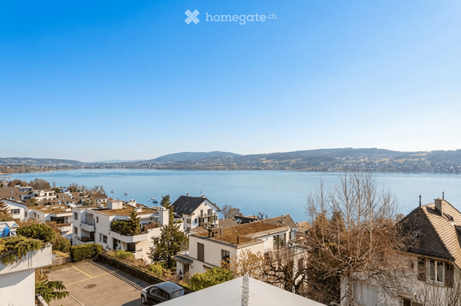 Houses with lake view, mountains in the background, parking lot, trees