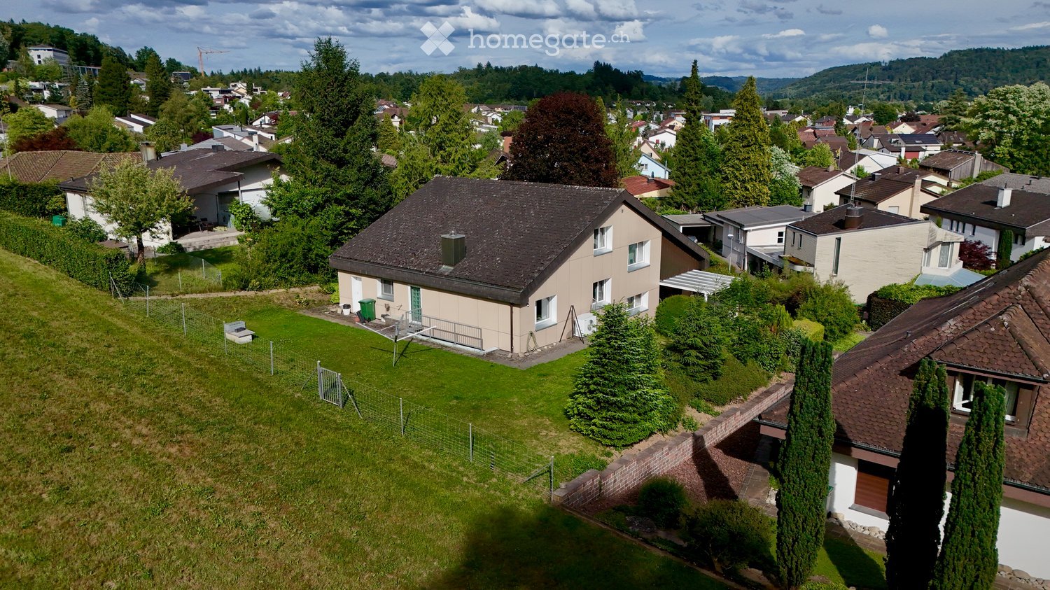 Aerial view of a residential house with a well-maintained lawn, surrounded by trees and neighboring houses in a suburban area.