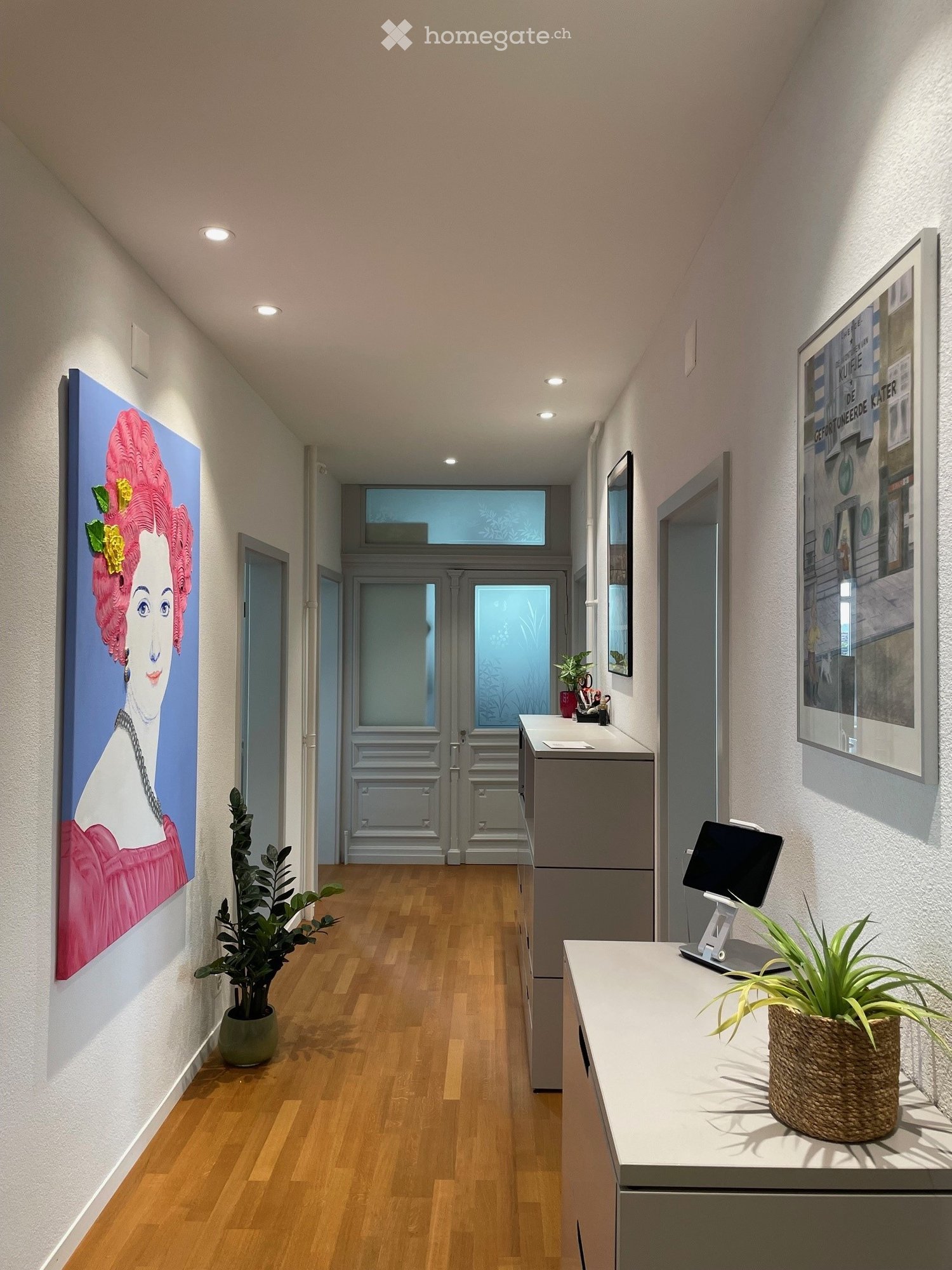 wooden floor, white walls, wooden hallway leading to the living room, 2 paintings, 2 potted plants, cabinet with drawers