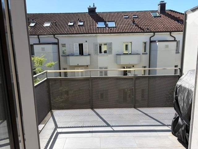 Balcony with metal railing, tiled floor, and view of neighboring buildings with balconies and windows.