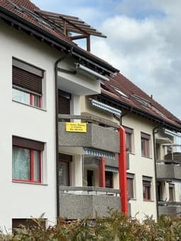 Multi-story residential building with white facade, multiple windows, balconies, and a visible entrance sign.