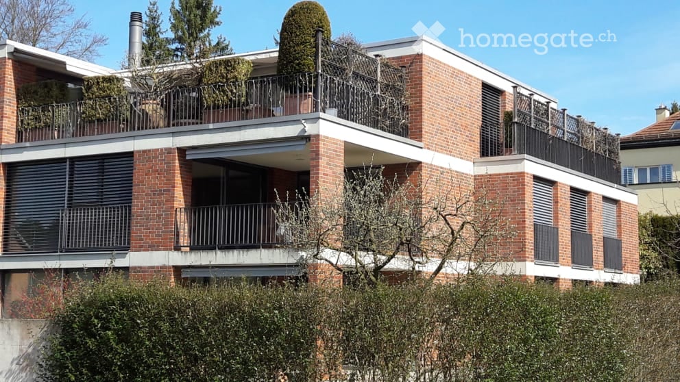 Modern brick apartment building with multiple balconies and greenery on the roof.