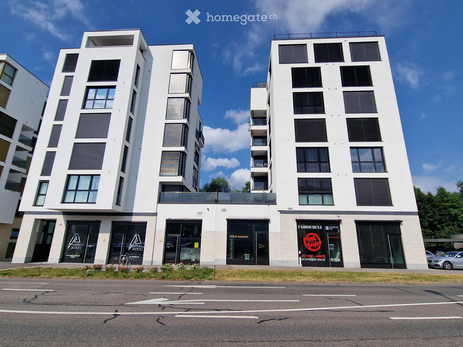 Modern multi-story building with white facade, large windows, and commercial storefronts at ground level.