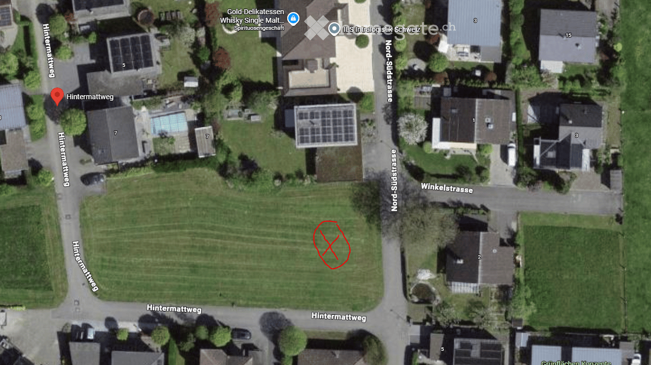 Aerial view of a residential area with multiple houses, green spaces, and a swimming pool visible in the neighborhood.