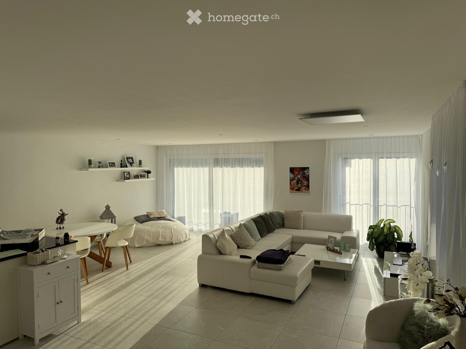 Bright living room with a large sectional sofa, coffee table, dining area with chairs and table, and decorative items including a plant and picture frames.