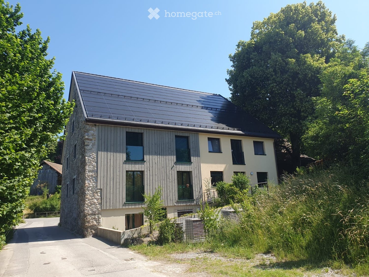 Two-story modern house with a combination of stone and wood exterior, large windows, and a sloped metal roof.