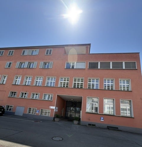 Multi-story building with red brick facade, multiple windows, and a central entrance. A parking sign is visible on the right side.
