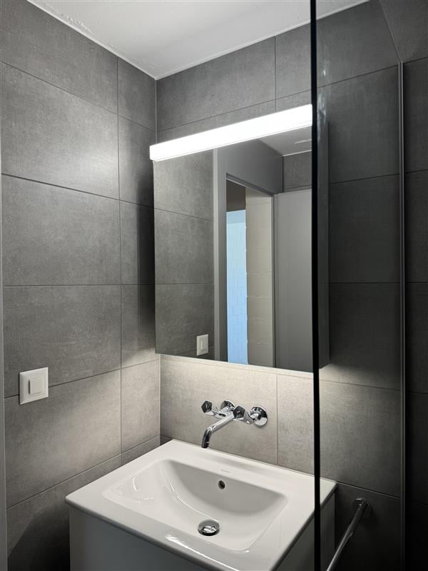 Bathroom. Modern bathroom with a white sink, chrome faucet, large mirror with built-in lighting, and grey tiled walls.