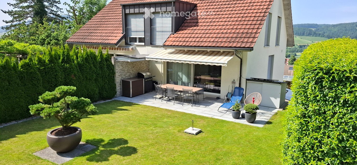 Well-maintained garden with a lawn, potted plants, outdoor dining set, and a covered patio area with a grill and seating.