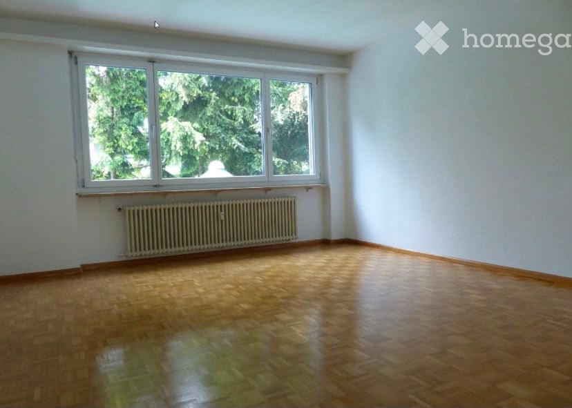 Empty room with wooden flooring, large window, radiator, and white walls.