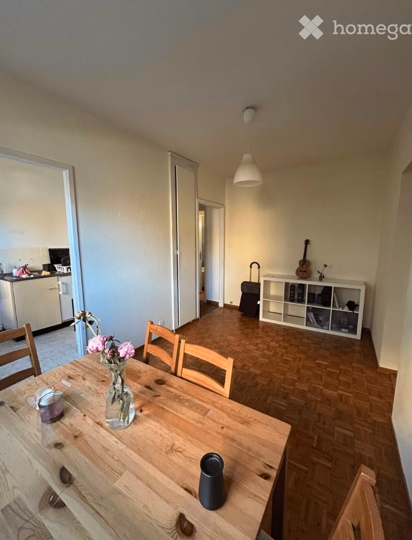 A well-lit dining area with a wooden table, chairs, a vase with flowers, and a guitar on a shelf. The room features wooden flooring and a modern aesthetic.