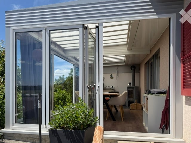 Modern balcony with large glass doors, wooden floor, and a small seating area with a table and chairs.
