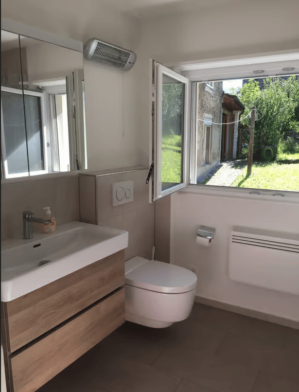 Modern bathroom with a sink, toilet, mirror, and a window offering a view of the garden.