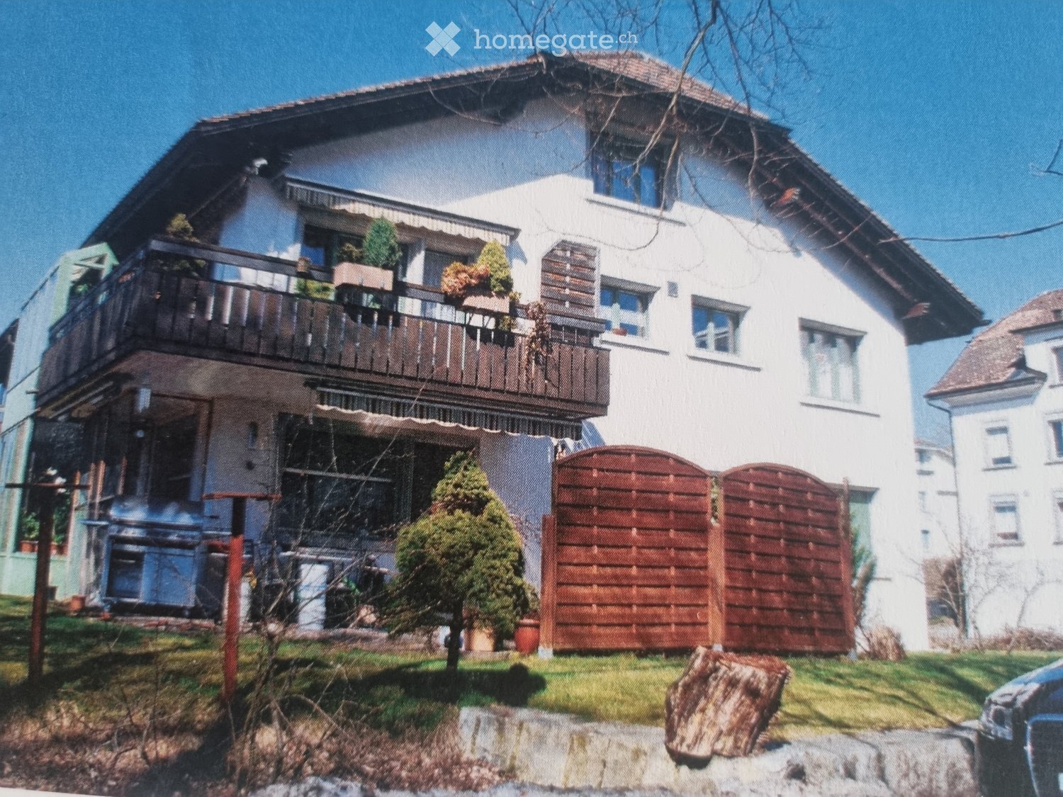 Two-story house with white exterior, multiple windows, balconies, and a wooden gate.