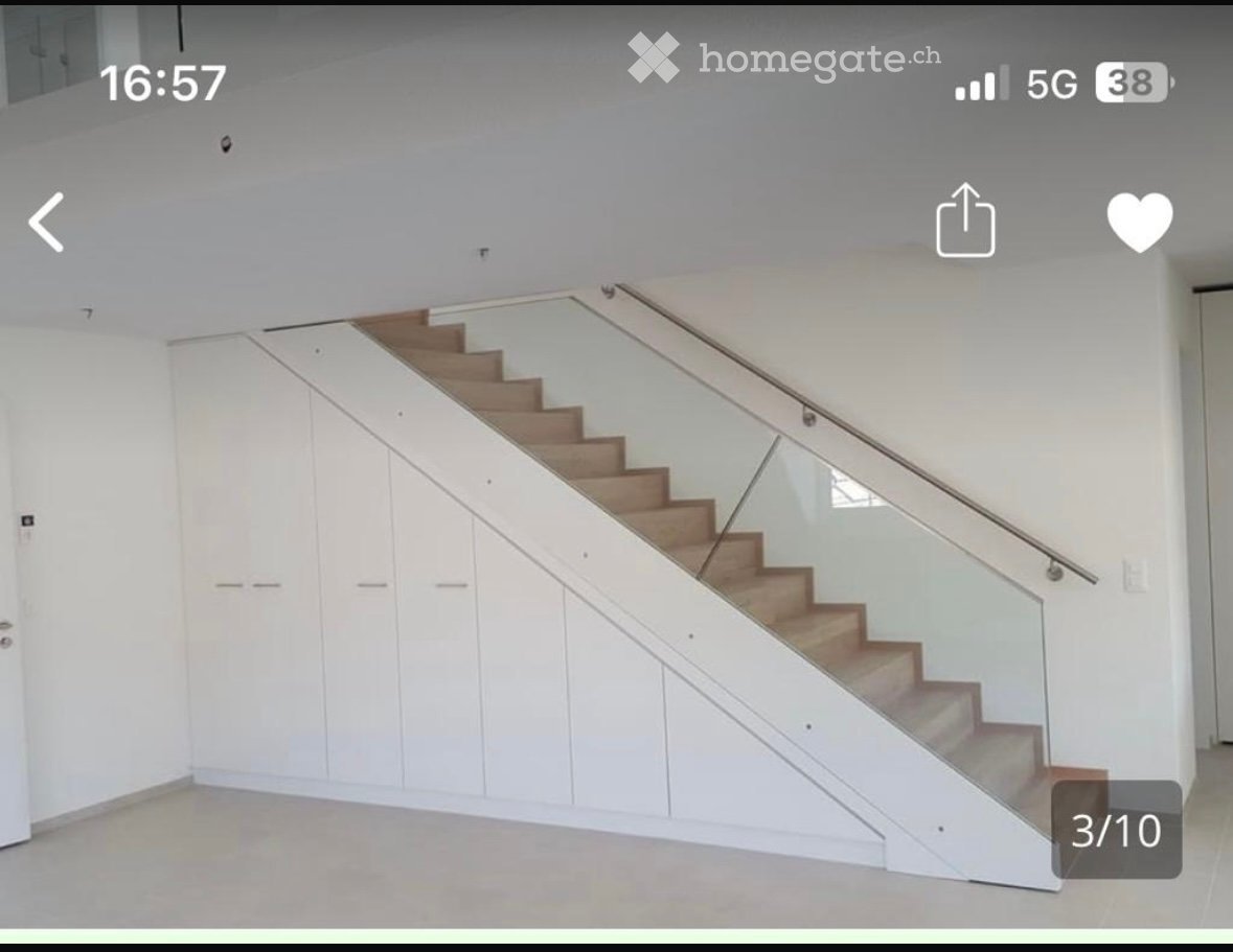 Modern staircase with wooden steps and glass railing, white built-in storage cabinets on one side, light-colored walls and floor.